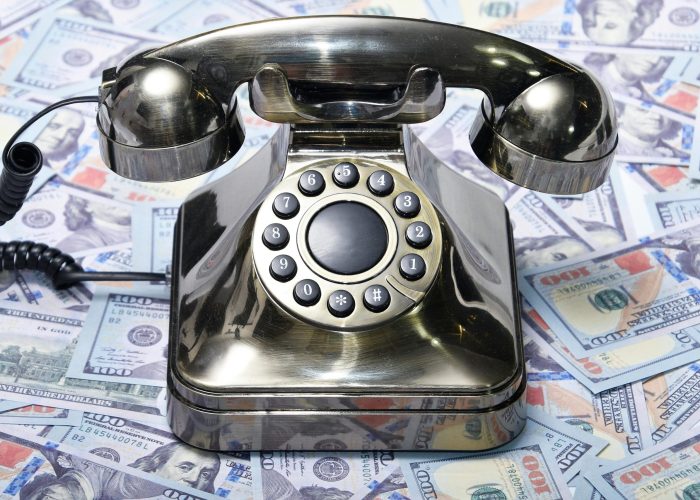 A retro rotary phone placed on a pile of US dollar bills, symbolizing communication and finance.