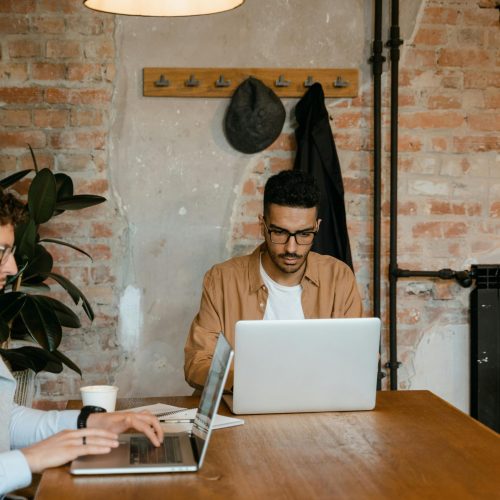 Two men working on laptops in a stylish office with exposed brick walls.
